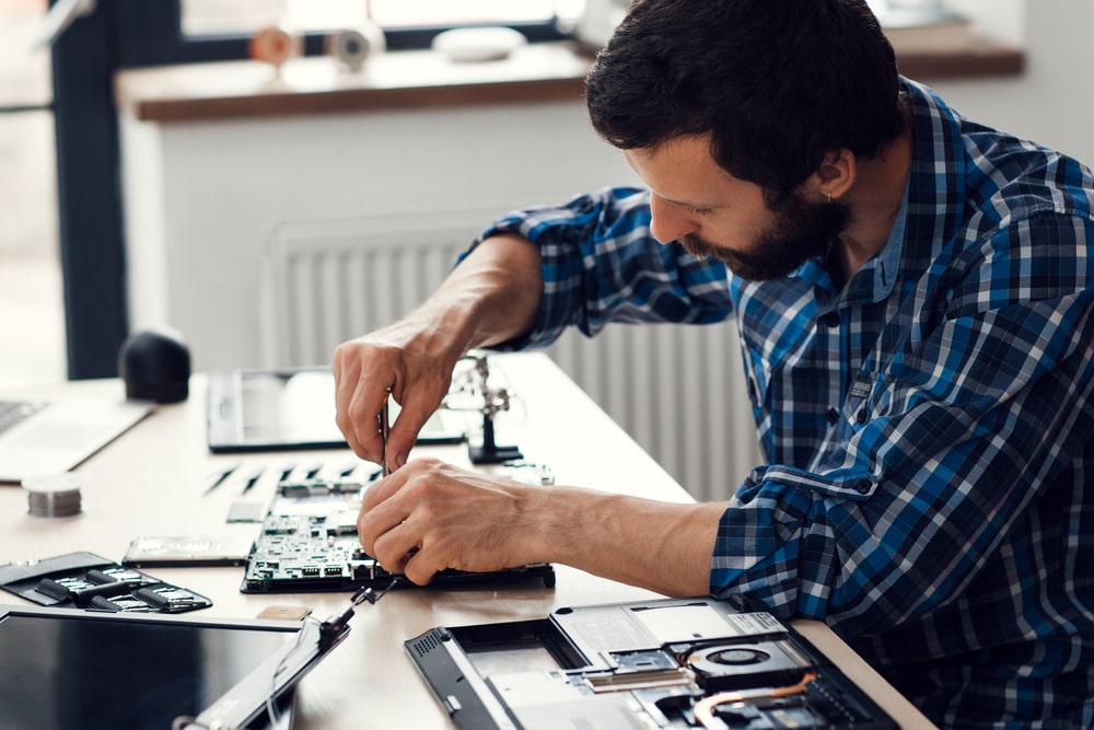 Side view of a dismantled laptop being repaired by an engineer, highlighting the importance of maintenance in the audio visual equipment supplier industry.